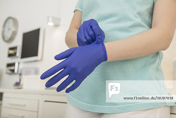 Mid section view of a female dental assistant putting on surgical gloves for treatment  Munich  Bavaria  Germany