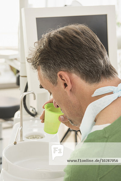 Zahnärztlicher Patient spuckt in ein Mundspülbecken in der Zahnarztpraxis  München  Bayern  Deutschland
