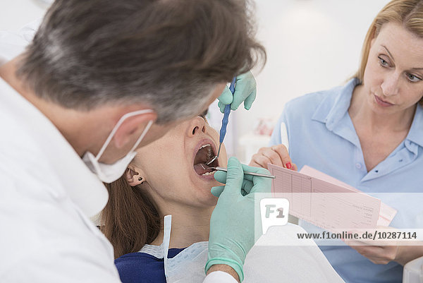 Zahnarzt  der den Patienten untersucht und den Befund der Assistentin diktiert  München  Bayern  Deutschland