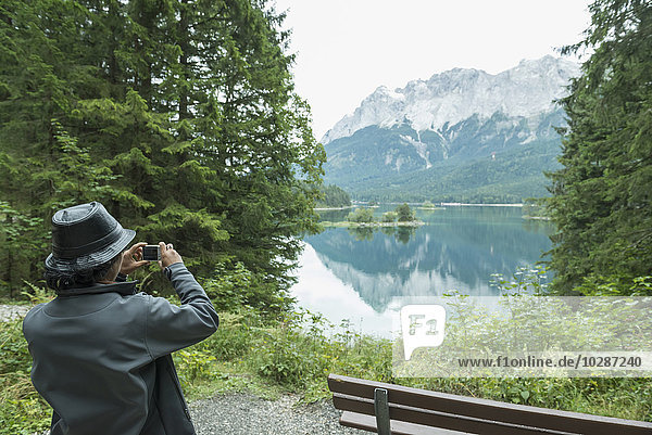 Rückansicht eines Touristen  der ein Foto mit einer Kamera am Eibsee  Bayern  Deutschland  macht