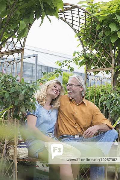 Mature couple sitting on a bench and smiling in plant nursery  Augsburg  Bavaria  Germany