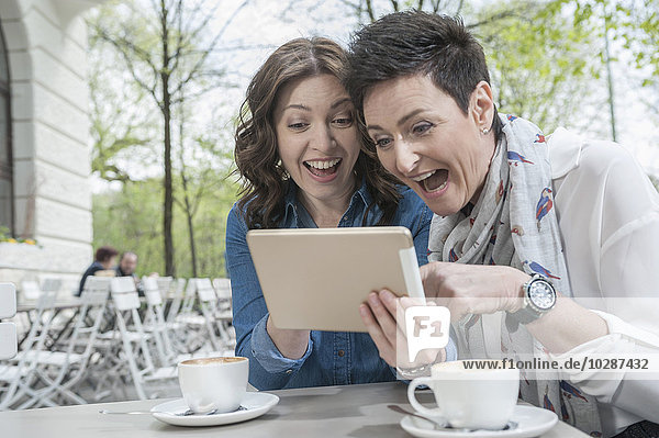 Zwei Freunde benutzen ein digitales Tablet in einem Straßencafé  Bayern  Deutschland