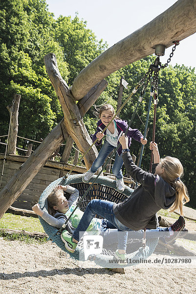 Three girls swinging on a swing in playground  Munich  Bavaria  Germany