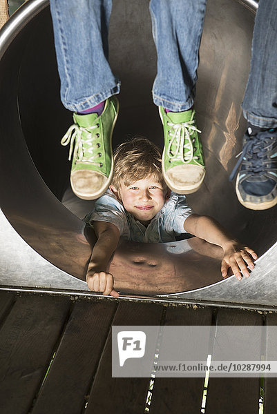Junge rutscht in einer Tunnelrutsche mit zwei Kindern  die ihre Füße baumeln lassen  München  Bayern  Deutschland