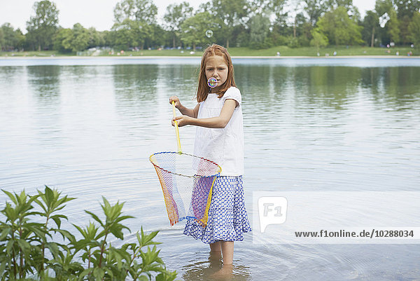 Mädchen fängt Seifenblasen mit Fischernetz im See  Bayern  Deutschland