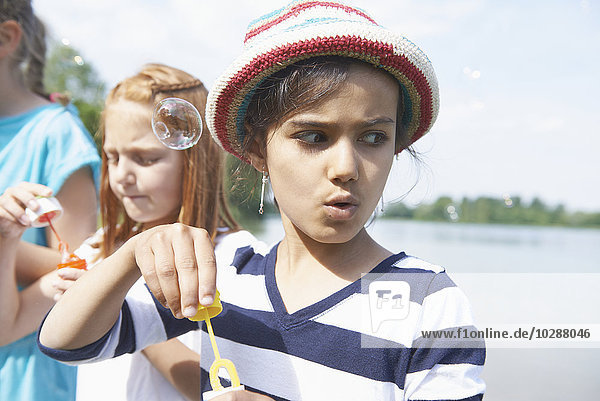 Mädchen blasen Seifenblasen mit Seifenblasenstäben am Seeufer  Bayern  Deutschland