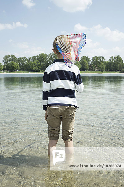 Rückansicht eines Jungen  der einen Brailer in den See hält  Bayern  Deutschland