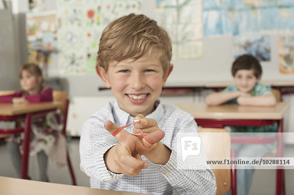 Schoolboy with a slingshot and smiling in classroom  Munich  Bavaria  Germany