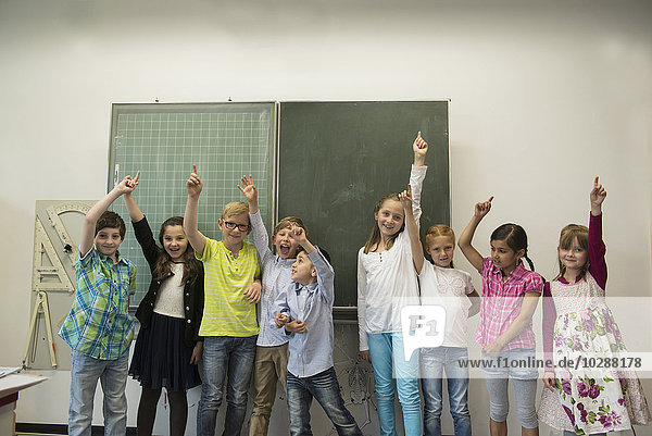 Schüler heben die Hände vor der Tafel im Klassenzimmer  München  Bayern  Deutschland