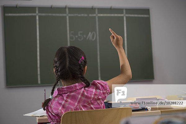 Schülerin vor der Tafel mit erhobener Hand im Klassenzimmer,  München,  Bayern,  Deutschland