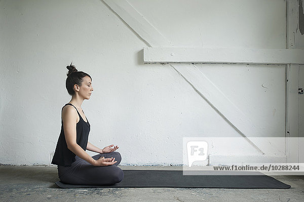 Seitenprofil einer mittelgroßen erwachsenen Frau  die in einem Yogastudio den Lotussitz übt  München  Bayern  Deutschland