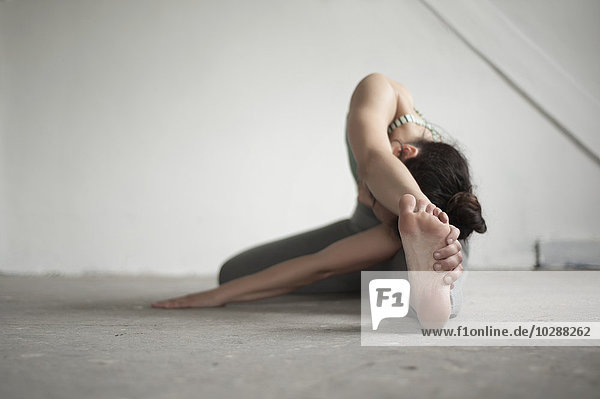 Mid adult woman practicing janu sirsasana pose in yoga studio  Munich  Bavaria  Germany