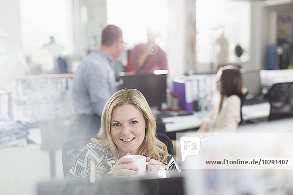 Portrait lächelnder Modedesigner beim Kaffeetrinken am Computer im Büro