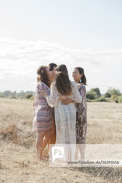 Boho women hugging in a circle in sunny rural field
