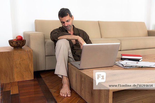 Barfuss reifer Mann auf Holzboden sitzend mit Laptop  Blick nach unten