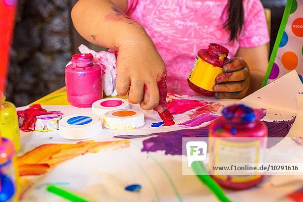 Mädchen sitzt am Tisch  macht Kunst  benutzt Farbe  konzentriert sich auf Kunstwerke