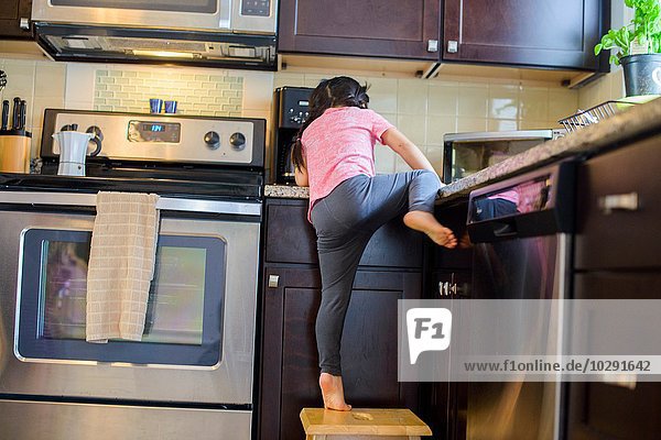 Junges Mädchen klettert vom Hocker auf die Küchenarbeitsfläche  Rückansicht