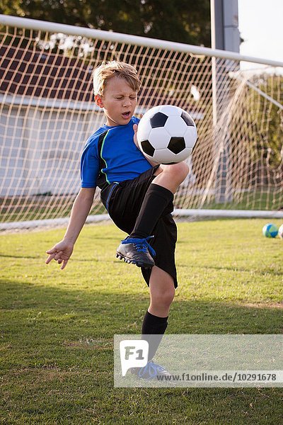 Junge spielt keepy uppy mit Fußball auf dem Spielfeld