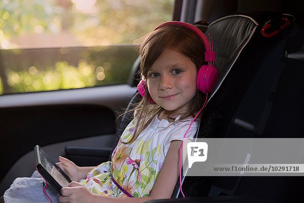 Porträt eines Mädchens mit rosa Kopfhörern und digitalem Tablett im Auto