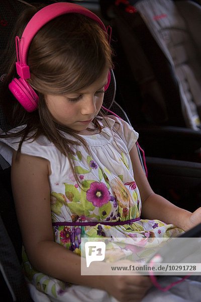 Mädchen mit rosa Kopfhörern konzentriert sich auf digitales Tablett im Auto