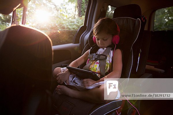 Mädchen mit Kopfhörer mit digitalem Tablett auf dem Rücksitz im Auto