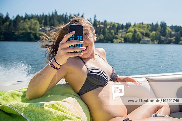 Young woman wearing bikini taking smartphone selfie on motor boat  Lake Oswego  Oregon  USA