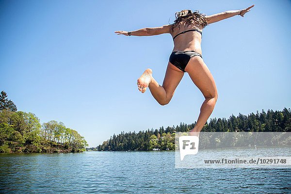 Rear view of young woman jumping into Lake Oswego  Oregon  USA