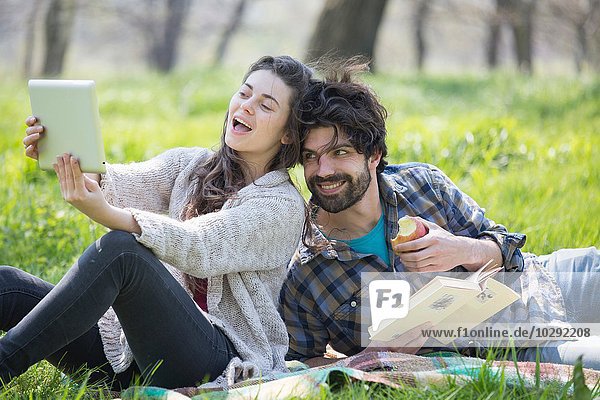 Junges Paar auf Picknickdecke mit digitalem Tablett Selfie im Wald