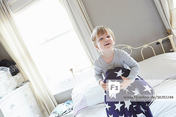 Junge auf dem Bett  der sich hinter einer marineblauen Wolldecke mit Sternenmuster hält.