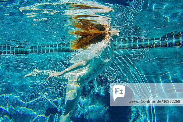 Junge Frau,  die unter Wasser schwimmt und ein dünnes weißes Hemd trägt.