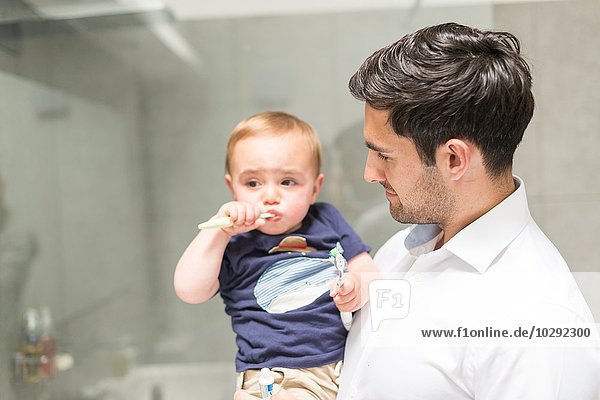 Father holding young son while son brushes teeth