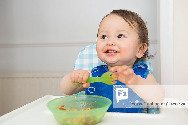 Baby boy eating baby food in kitchen high chair