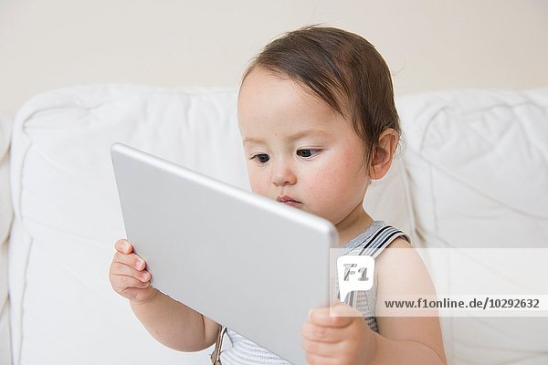 Baby boy sitting on sofa holding up digital tablet