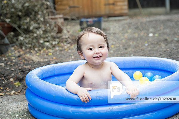 Portrait of cute baby boy sitting in garden paddling pool