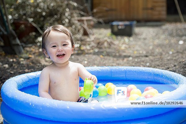 Portrait of cute baby boy playing in garden paddling pool