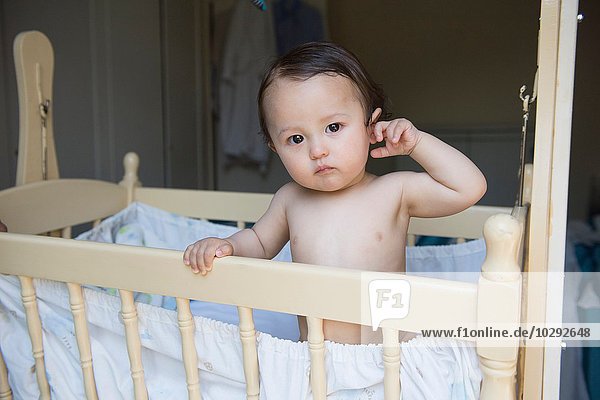 Portrait of tired baby boy standing in crib