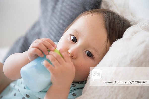 Portrait of baby boy on sofa drinking from baby cup