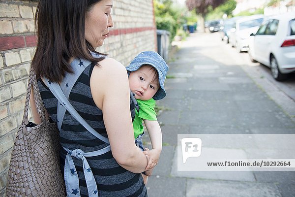 Portrait of baby boy being carried by mother in baby sling along street
