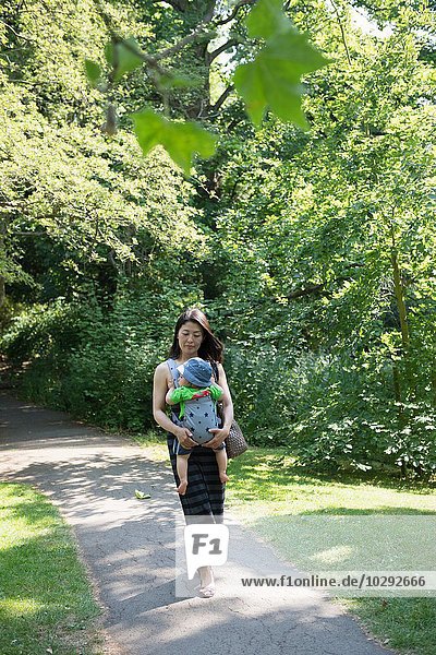 Mature mother and son in baby sling strolling in park