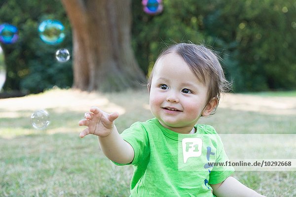Portrait of cute baby boy reaching for bubbles in park