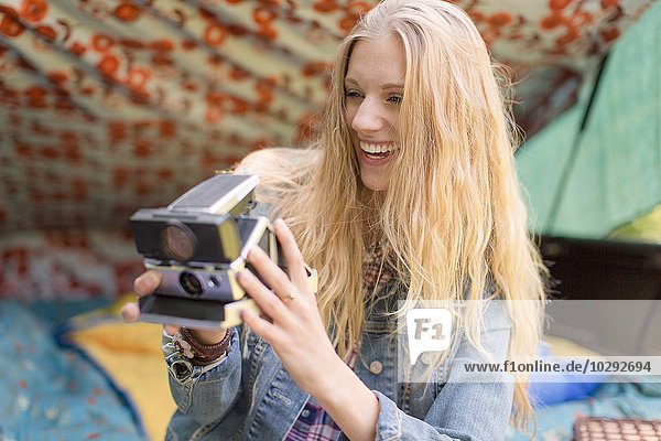 Junge Frau beim Fotografieren mit Sofortbildkamera beim Zelten