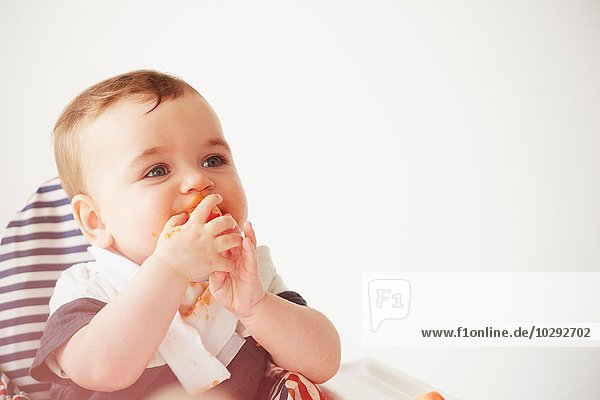 Baby Junge füttert sich im Kinderstuhl