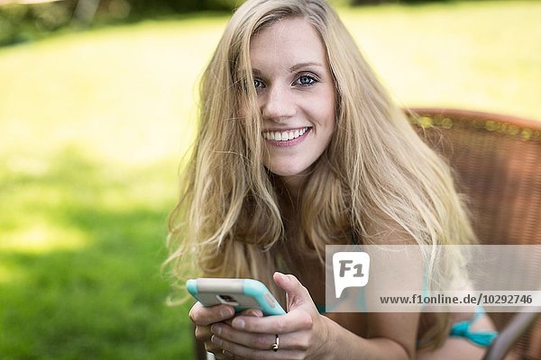 Portrait einer jungen Frau im Bikini mit Smartphone im Garten