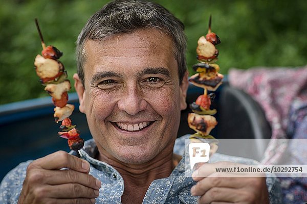 Porträt eines reifen Mannes mit gegrillten Kebabstäbchen