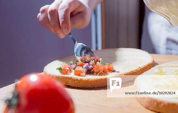 Hands of woman spreading ingredients on bread at kitchen counter