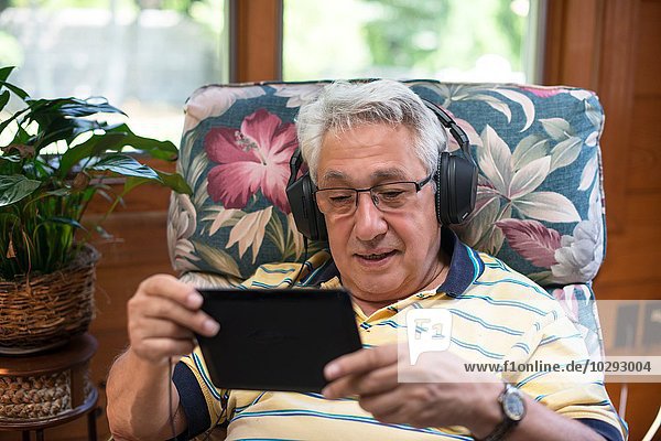 Senior Mann  zu Hause sitzend  Kopfhörer tragend  mit digitalem Tablett