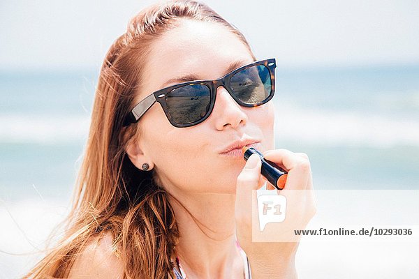Portrait of mid adult woman on beach  wearing sunglasses  applying lipstick