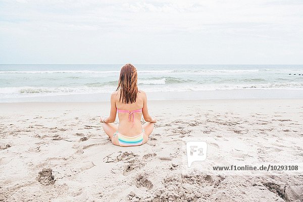 Mittlere erwachsene Frau beim Meditieren am Strand  Rückansicht