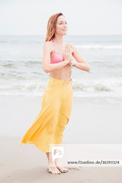Mittlere erwachsene Frau beim Meditieren am Strand  Hände zusammen