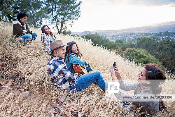Young woman photographing her four adult siblings on grassy hill